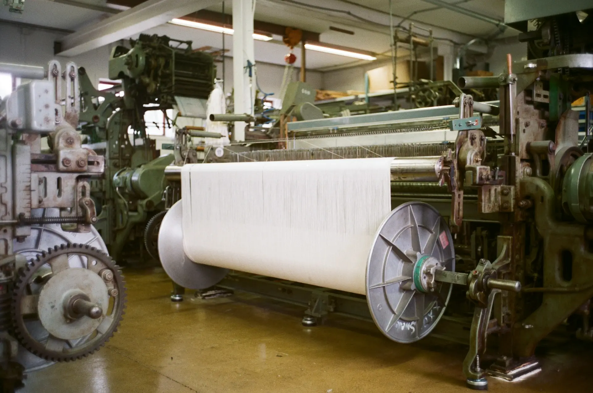 Industrial weaving looms with a large spool of white yarn in a textile mill